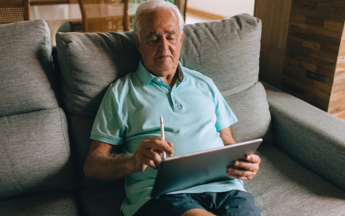 Elderly Man Sitting on Sofa with Tablet in Hands
