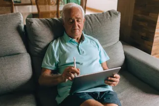Elderly Man Sitting on Sofa with Tablet in Hands