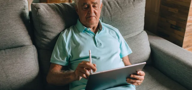 Elderly Man Sitting on Sofa with Tablet in Hands